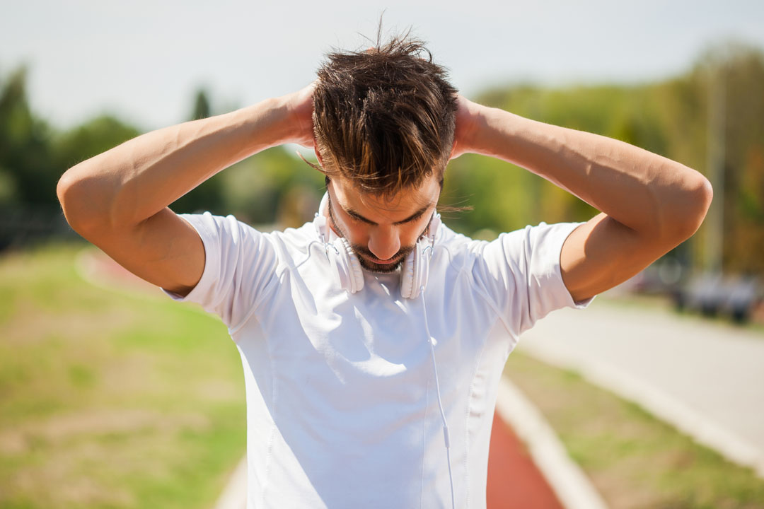 Young man is exercising on sunny day. He is stretching his neck.