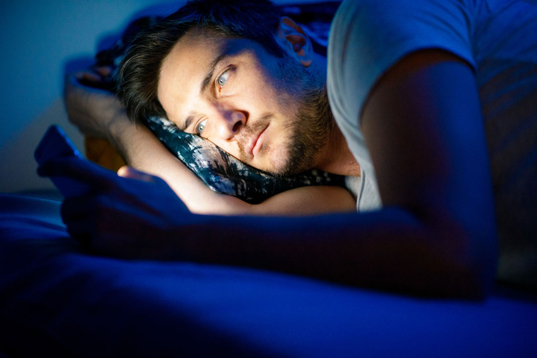 Young man using smart phone in bed at night, copy space