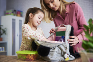 Young mum and daughter packing backpack for the school - healthy foods