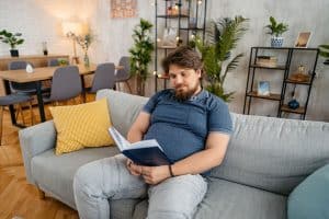 man sitting on couch reading a book at home - active vs sedentary lifestyle - heart disease