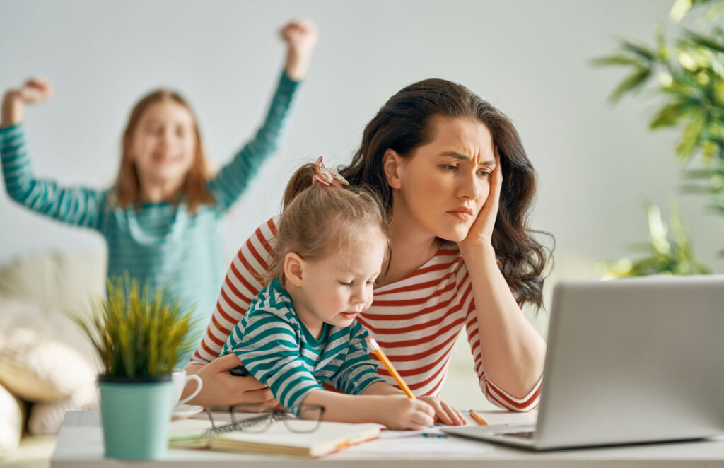 Woman working on a laptop with kids at home - Ways to ease stress and anxiety