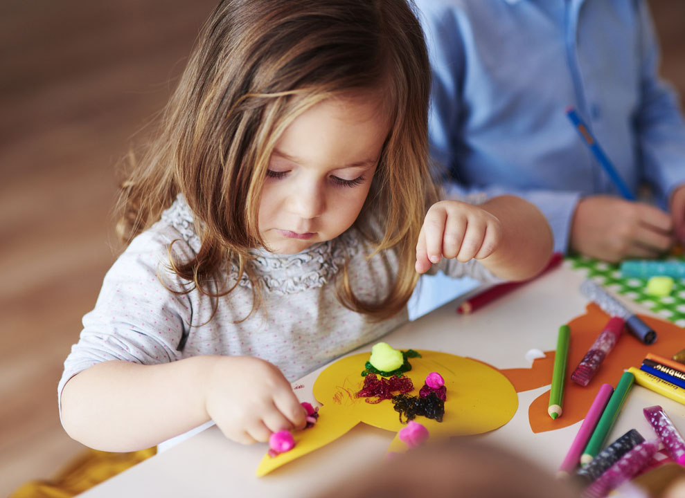 young girl doing DIY crafts from an idea box with pom pom glitter and glue