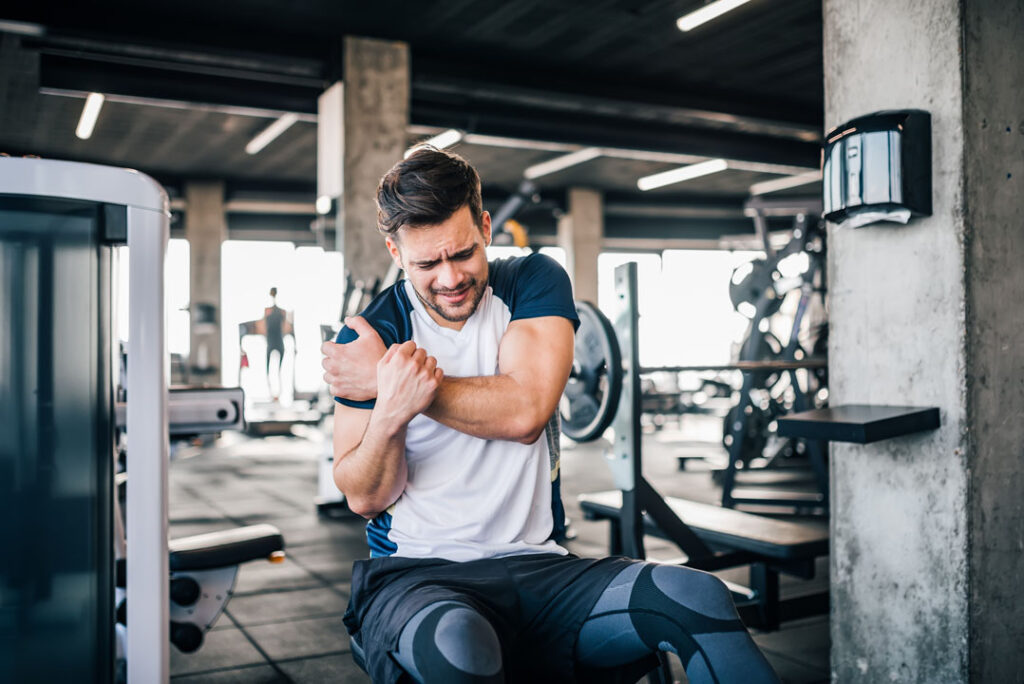 man working out in gym grabbing his shoulder from a sport injury