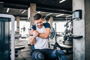 man working out in gym grabbing his shoulder from a sport injury