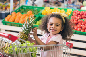 smiling kid sitting in shopping cart with pineapple in grocery store - pineapple for natural allergy relief