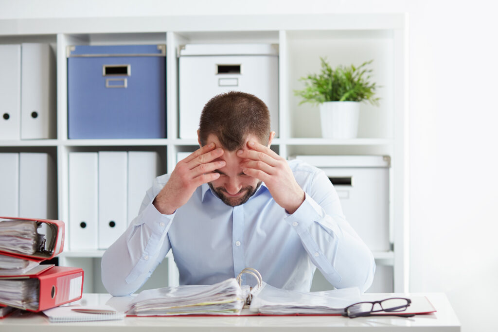 Young business man under stress with headache and migraine - sitting at desk for long periods of time - reasons for an afternoon slump