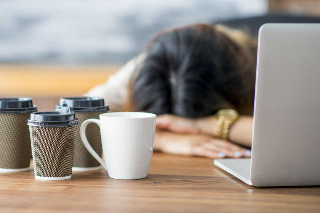 A female entrepreneur and businesswoman is working on her start up company in her office. She has fallen asleep at the office with her head on her desk. Empty coffee cups are on the table.