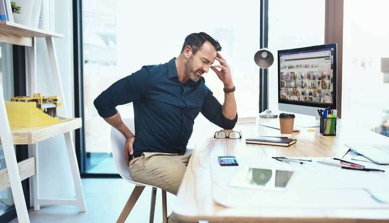 Shot of a mature businessman experiencing back pain while working at his desk with bad posture