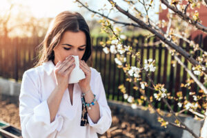 seasonal spring allergies - woman sneezing into a tissue - spring flowers