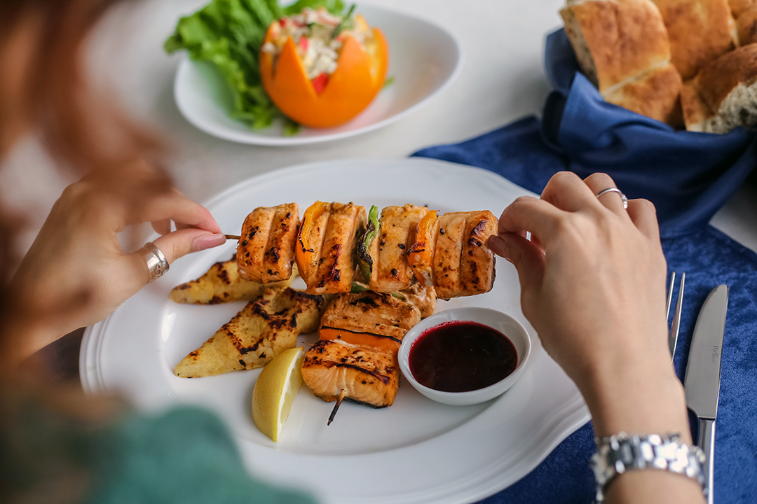 protein - side view woman eating grilled fish on skewers with sauce and lemon on a plate and bread on the table