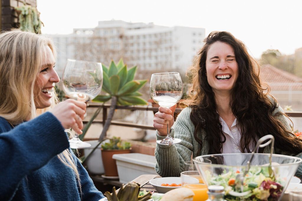 Happy young friends drinking and toasting white wine at dinner p