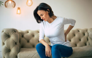 Woman sitting on a couch and holding her lower back