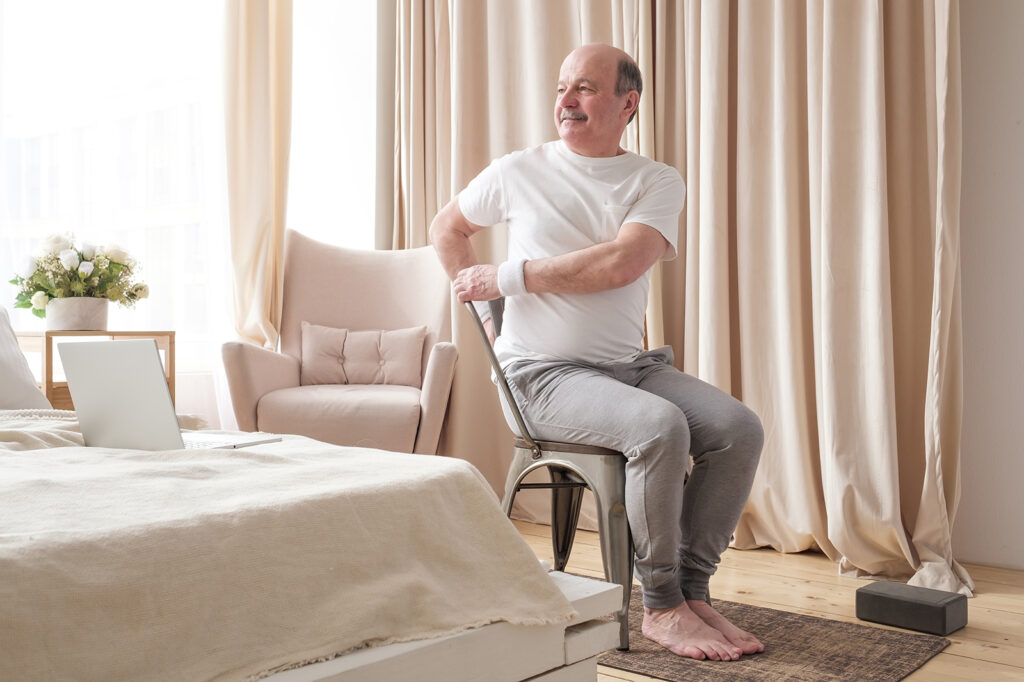 Sporty senior man practicing yoga using chair, doing Parivrtta Utkatasana