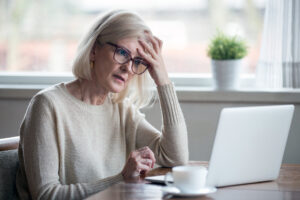 confused mature woman with brain fog sitting at laptop