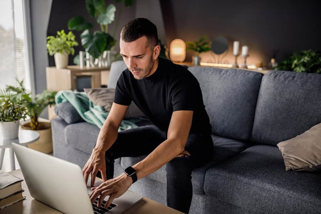 man working at home on couch typing into his laptop - office ergonomics
