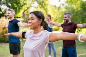 Mixed race woman exercising in park with mature friends - boosting energy