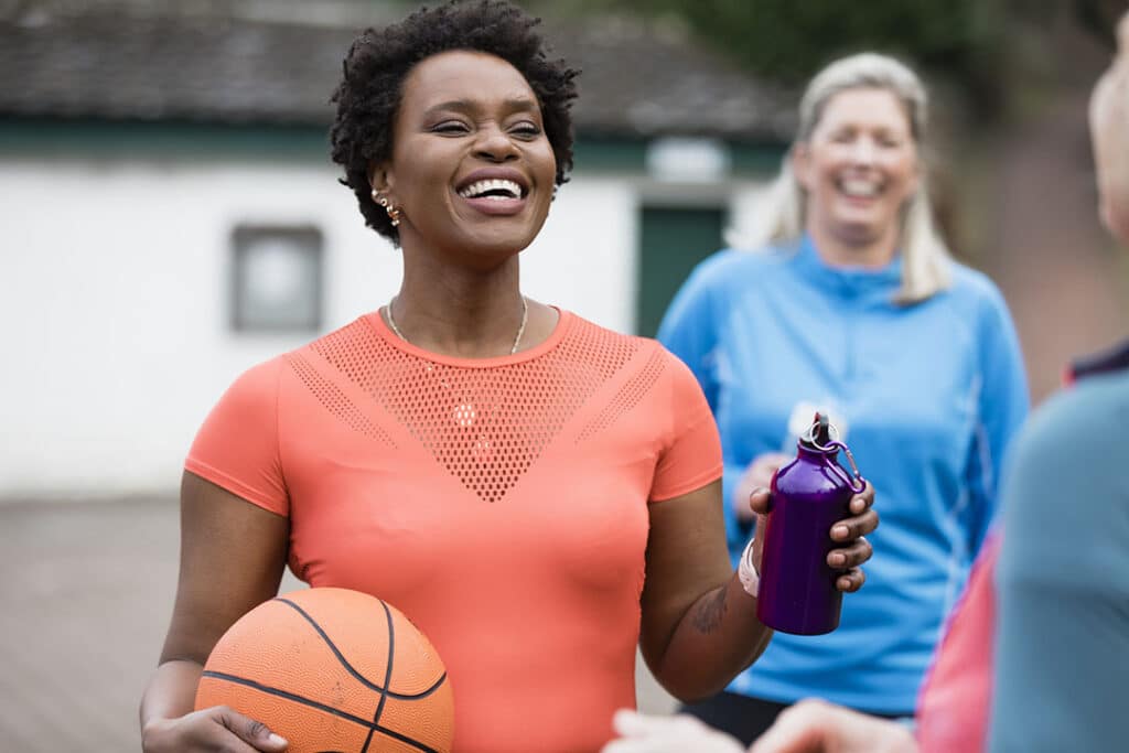 Mature women standing around in a public park having a conversation and laughing after a game of Netball - boosting energy through exercise