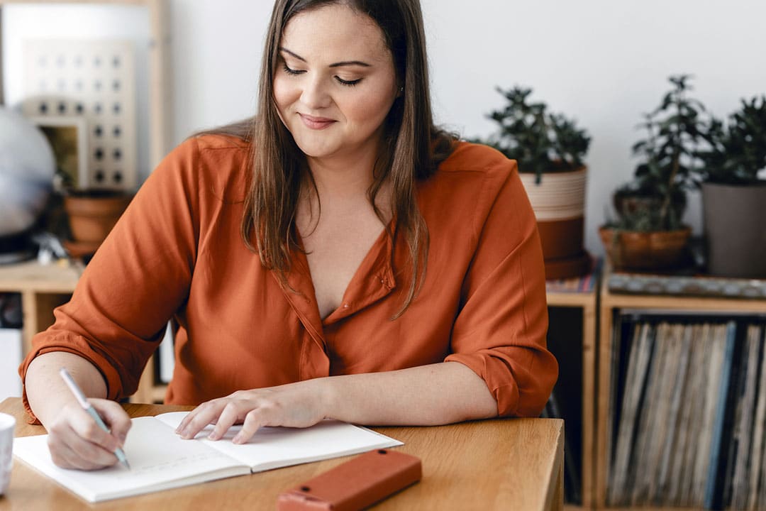 https://alignlife.com/wp-content/uploads/2022/11/AlignLife_Articles_Smiling-plus-size-woman-sitting-at-her-desk-and-writing-a-journal_iStock-1299495999.jpg