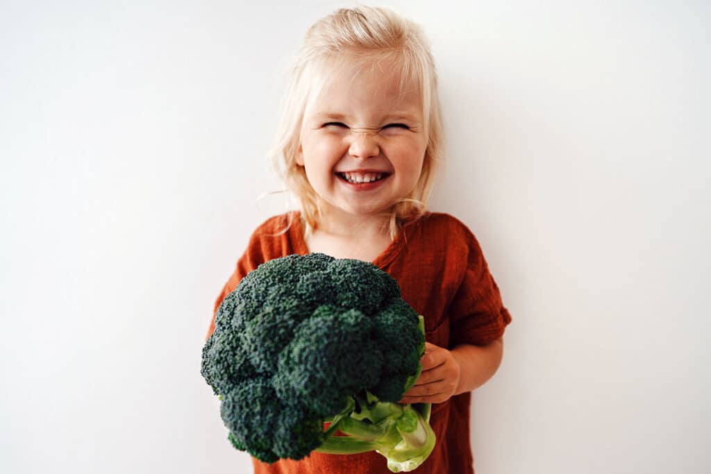 little girl holding broccoli - trying new foods - winning over picky eater