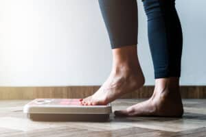 woman stepping on to scale to check weight goals - weight gain - weight loss