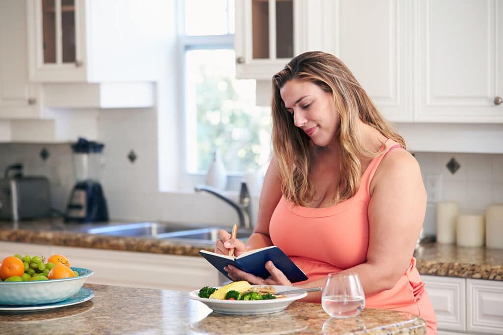 Curvy woman updating her food journal to track any food sensitivities and weight loss goals