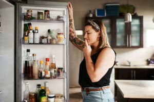 young woman search refrigerator for healthy foods - vitamin deficiency and the foods we eat