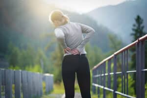 woman massaging her low back while exercising outdoors - low back pain and tight hip flexors