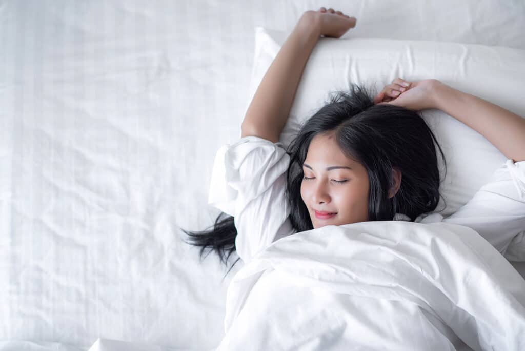 woman waking up happy in her bedroom - best sleeping positions - best pillow for sleep