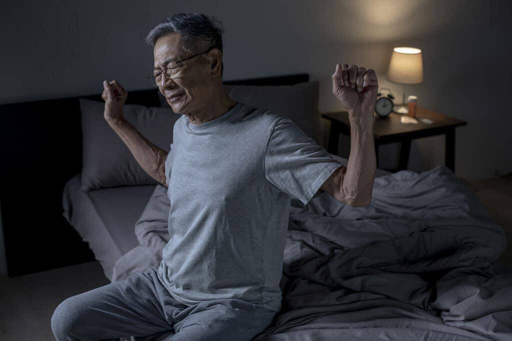 senior man sitting on side of bed with back pain at night