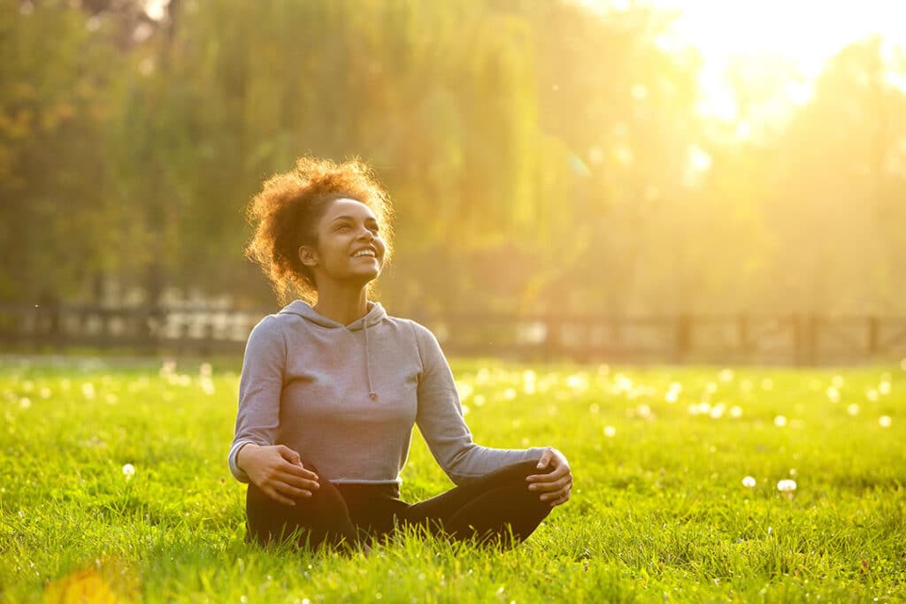 You woman smiling outdoors doing yoga - Ways to increase serotonin naturally - AlignLife