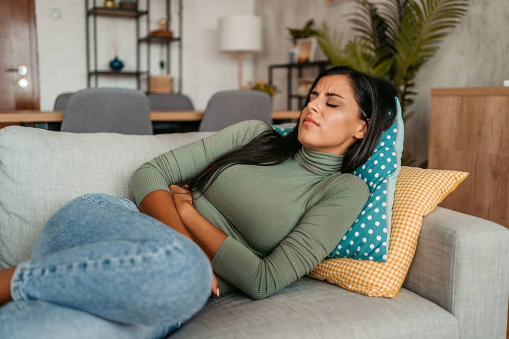 Young woman lying on the couch with stomach cramps - Spine Wellness - Spine to Symptoms