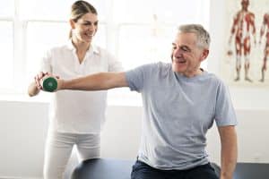 Senior man doing strengthening exercises on shoulder with physical therapist