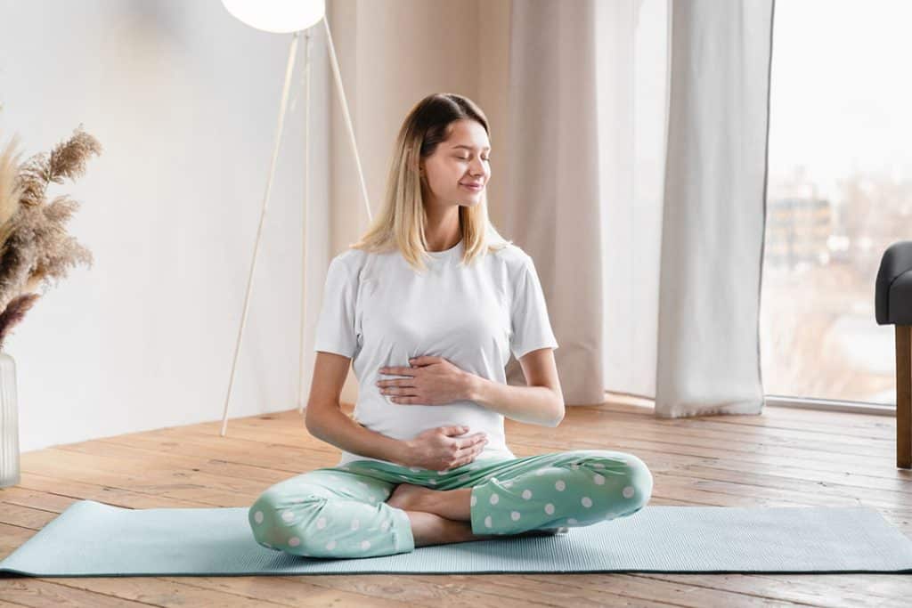 Pregnant woman sitting on yoga mat in living room - gut health during pregnancy