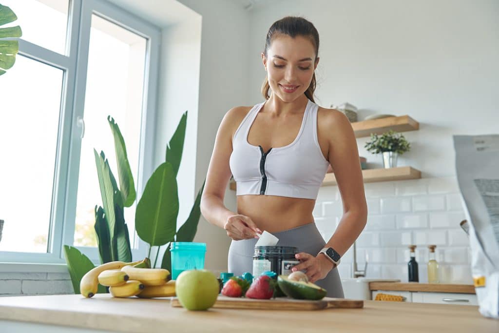 young woman making protein shake in kitchen - how to boost your metabolism