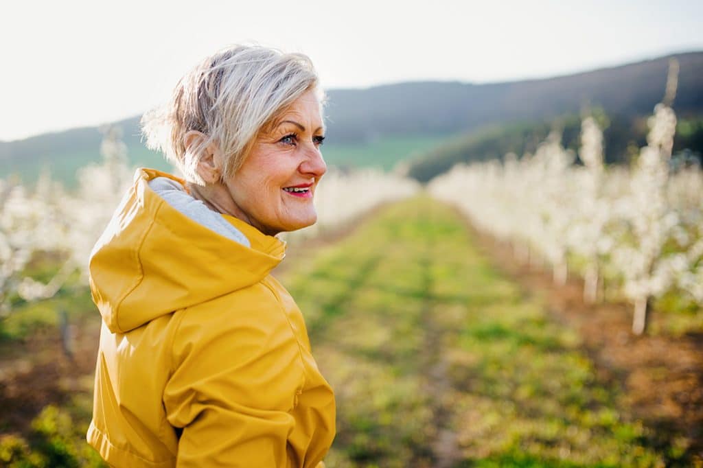 senior woman walking in an orchard - spring wellness