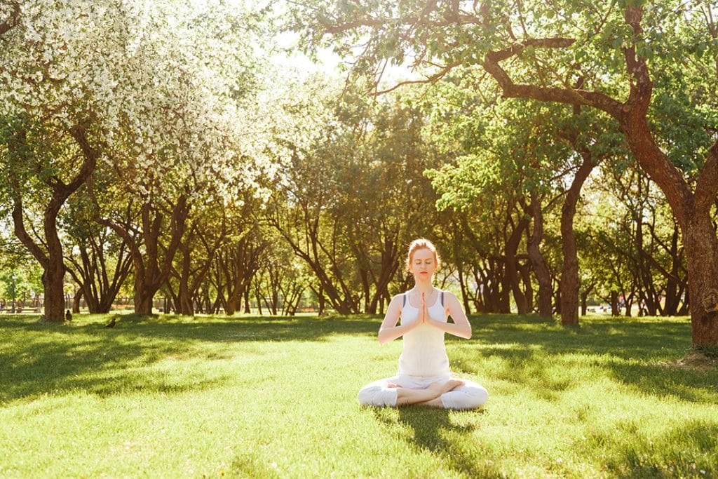 Young red hair woman peacefully meditating in park - spring cleaning bad habits - creating healthy habits