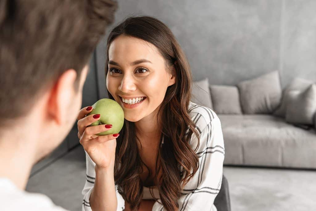 Woman eating an apple smiling - lasting relief from TMJ and jaw pain