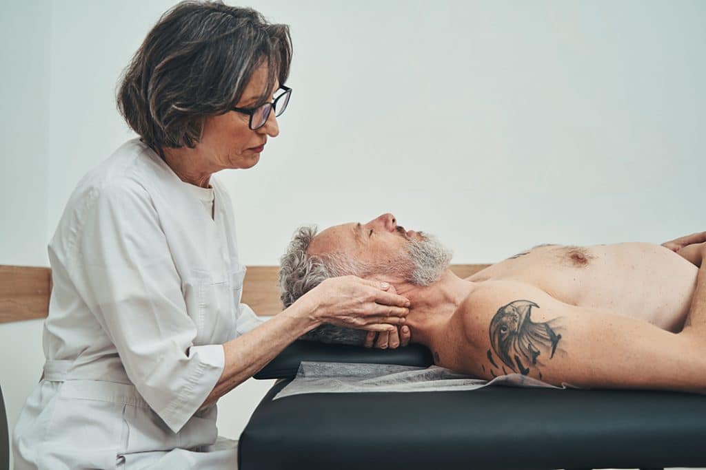 Focused female chiropractor conducting the osteopathic manipulative treatment on a male patient to help relieve jaw pain from TMJ