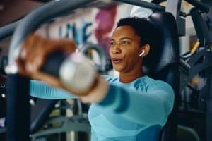 Black sportswoman doing chest exercises on machine while working out in gym - reason to do strength training