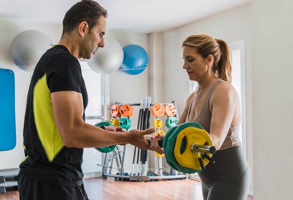 Coach teaching a woman how to do weights in a gym - how to start a strength training program