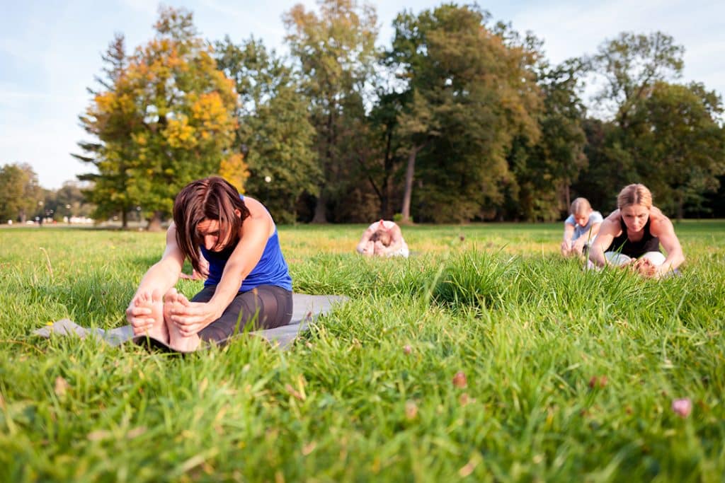 mixed group of people practicing yoga doing a leg stretch to prevent leg cramps