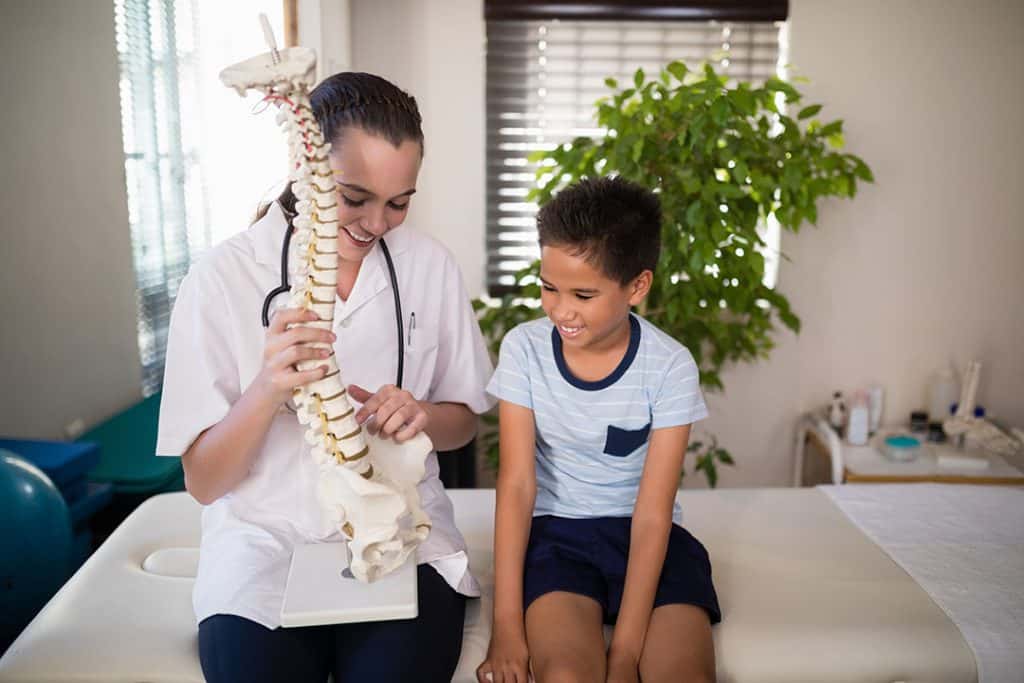 Female chiropractor talking with a boy while she is holding a 3d spine