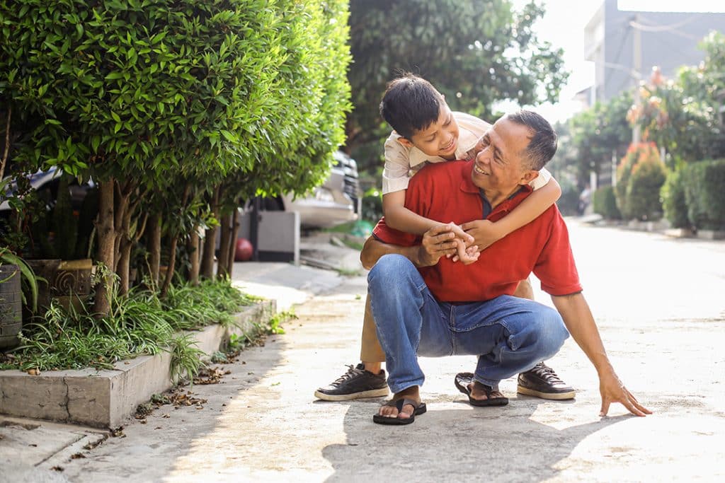 Grandpa crouched own on the ground outside with grandson on his back - good low back mobility