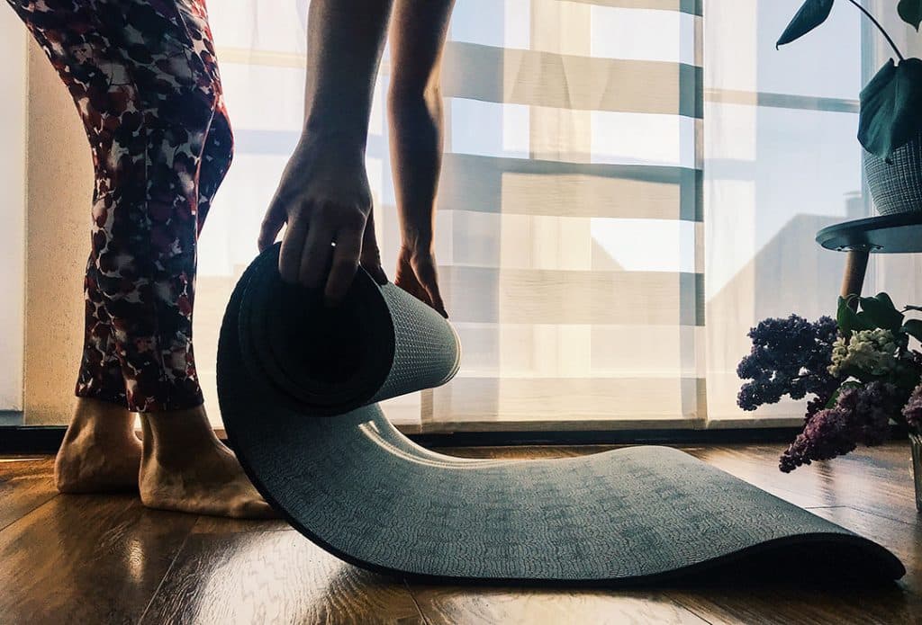 Woman rolling out yoga mat at home for daily exercises