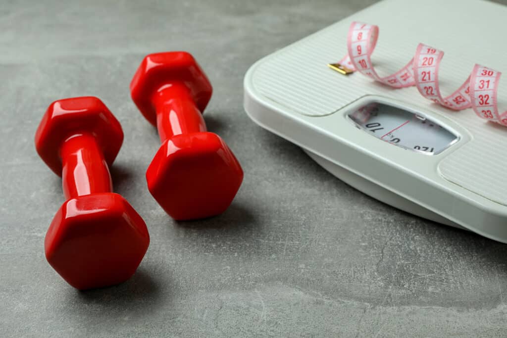 Scales, dumbbells and measuring tape on gray background with a scale - exercise for weight loss