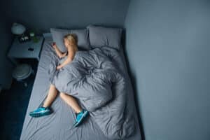 Woman laying in bed with exercise shoes on her feet. Sleep vs exercise