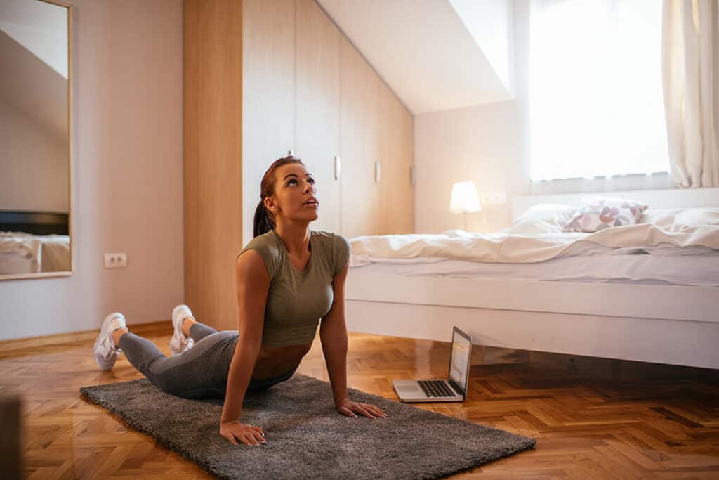 Woman doing yoga stretches at home in bedroom - sleep vs exercise