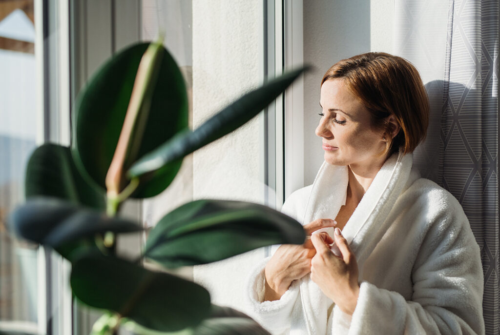 woman standing by a window in a robe - immune-boosting morning habits