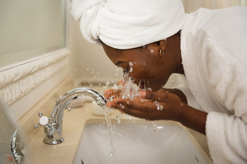 Woman washing face in bathroom with cold water - immune boosting habits