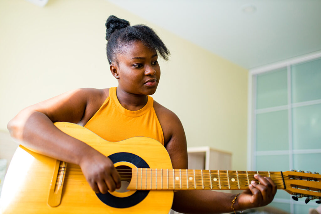 teenage girl practicing her skill on acoustic guitar .- benefits of reducing screen time